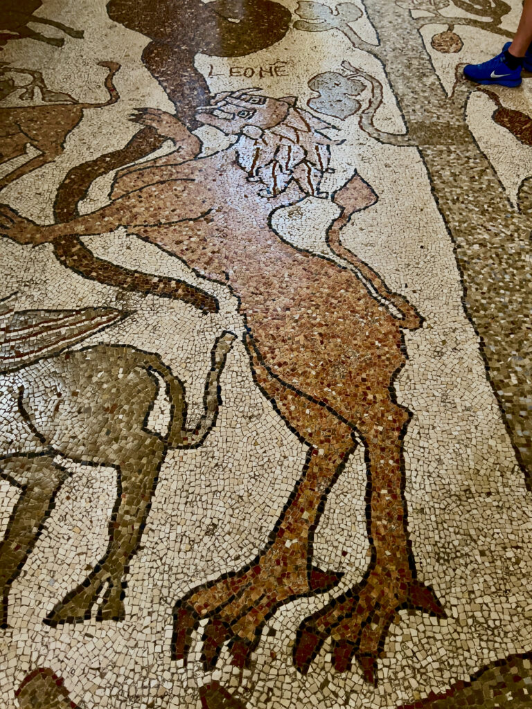 Inside Otranto Cathedral is one of the largest and best preserved medieval floor mosaics in Europe. The mosaic, which spans the length of the central nave and parts of the side naves, consists of around 10 million individual tiles. It was completed in only three years, in 1166, by the monk Pantaleone of San Nicola di Casole monastery.

Depicting the Tree of Life, three allegorical trees serve as an ancient Wikipedia, encompassing themes from the Holy Scriptures such as Genesis, the Flood, Solomon and the Queen of Sheba, and scenes of Heaven and Hell. The mosaic includes representations of Ancient Roman bestiarii, months of the year, and mythological figures like Atlas with the globe on his shoulders. There are depictions from classical and Breton legends: Alexander the Great’s ascent to the heavens and King Arthur. This synthesis of Greek, Byzantine, and Norman cultural themes reflects Otranto’s cultural diversity, where Christianity and Judaism coexisted. The city hosted a vibrant Jewish community of 500 families in the 12th century.

Photo by the Puglia Guys, Puglia ambassadors. PugliaGuys.com