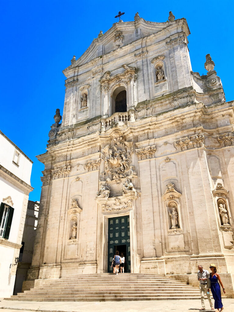 The basilica di San Martino, Martina Franca. From The Puglia Guys Martina Franca Guide.

Martina is a town rich in Baroque elegance, historic charm, and cultural heritage. Walking through its winding streets, visitors encounter stunning churches, grand palaces, and picturesque piazzas, each telling a story of the town’s rich past. Our Puglia Guys Martina Franca guide takes you on a journey through the most remarkable sites, from the Gothic convents to the Baroque splendor of its churches and palazzi, with recommendations for the best local restaurants to complete your experience

Nestled in the picturesque Valle d’Itria, approximately halfway between the Ionian and Adriatic Seas, Martina Franca’s strategic position—which allowed for control over trade and commerce, a key factor in the town’s prosperity—played a crucial role in shaping its past, from ancient settlements to medieval fortifications and Baroque splendour. 

For history lovers, art enthusiasts, and cultural explorers, Martina’s churches offer a glimpse into a time when faith and art were inextricably linked, creating monuments that continue to inspire and captivate.

Today, Martina Franca is a vibrant town, the largest of the Valle d’Itria. Its charm lies in its baroque architecture, splendid churches, the narrow streets of its old town, and 18th-century town houses with Baroque features and wrought-iron balconies. Known for its gastronomy (we recommend some of our favourite restaurants, but in reality there is no need to adhere to it, good food is easy to find) its best known culinary export capocollo di Martina Franca (our favourite regional cured meat).

Photo by the Puglia Guys, Puglia Travel ambassadors. PugliaGuys.com
