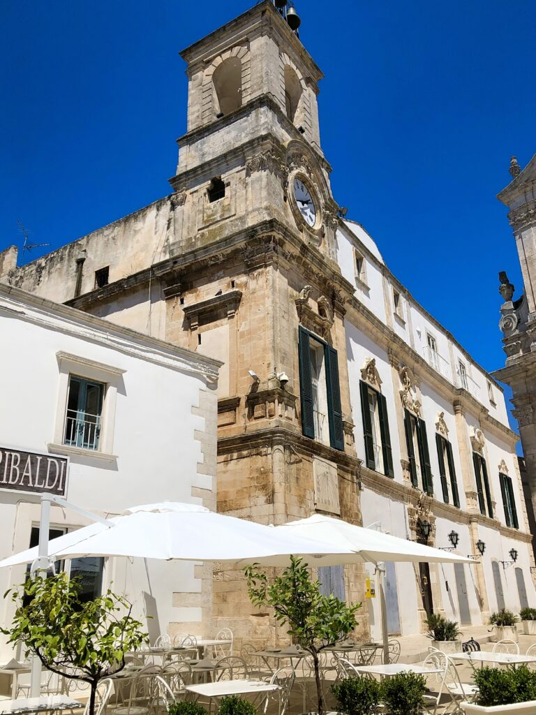 The civic clock tower on piazza Plebiscito, Martina Franca. From The Puglia Guys Martina Franca Guide.

Martina is a town rich in Baroque elegance, historic charm, and cultural heritage. Walking through its winding streets, visitors encounter stunning churches, grand palaces, and picturesque piazzas, each telling a story of the town’s rich past. Our Puglia Guys Martina Franca guide takes you on a journey through the most remarkable sites, from the Gothic convents to the Baroque splendor of its churches and palazzi, with recommendations for the best local restaurants to complete your experience

Nestled in the picturesque Valle d’Itria, approximately halfway between the Ionian and Adriatic Seas, Martina Franca’s strategic position—which allowed for control over trade and commerce, a key factor in the town’s prosperity—played a crucial role in shaping its past, from ancient settlements to medieval fortifications and Baroque splendour. 

For history lovers, art enthusiasts, and cultural explorers, Martina’s churches offer a glimpse into a time when faith and art were inextricably linked, creating monuments that continue to inspire and captivate.

Today, Martina Franca is a vibrant town, the largest of the Valle d’Itria. Its charm lies in its baroque architecture, splendid churches, the narrow streets of its old town, and 18th-century town houses with Baroque features and wrought-iron balconies. Known for its gastronomy (we recommend some of our favourite restaurants, but in reality there is no need to adhere to it, good food is easy to find) its best known culinary export capocollo di Martina Franca (our favourite regional cured meat).

Photo by the Puglia Guys, Puglia Travel ambassadors. PugliaGuys.com
