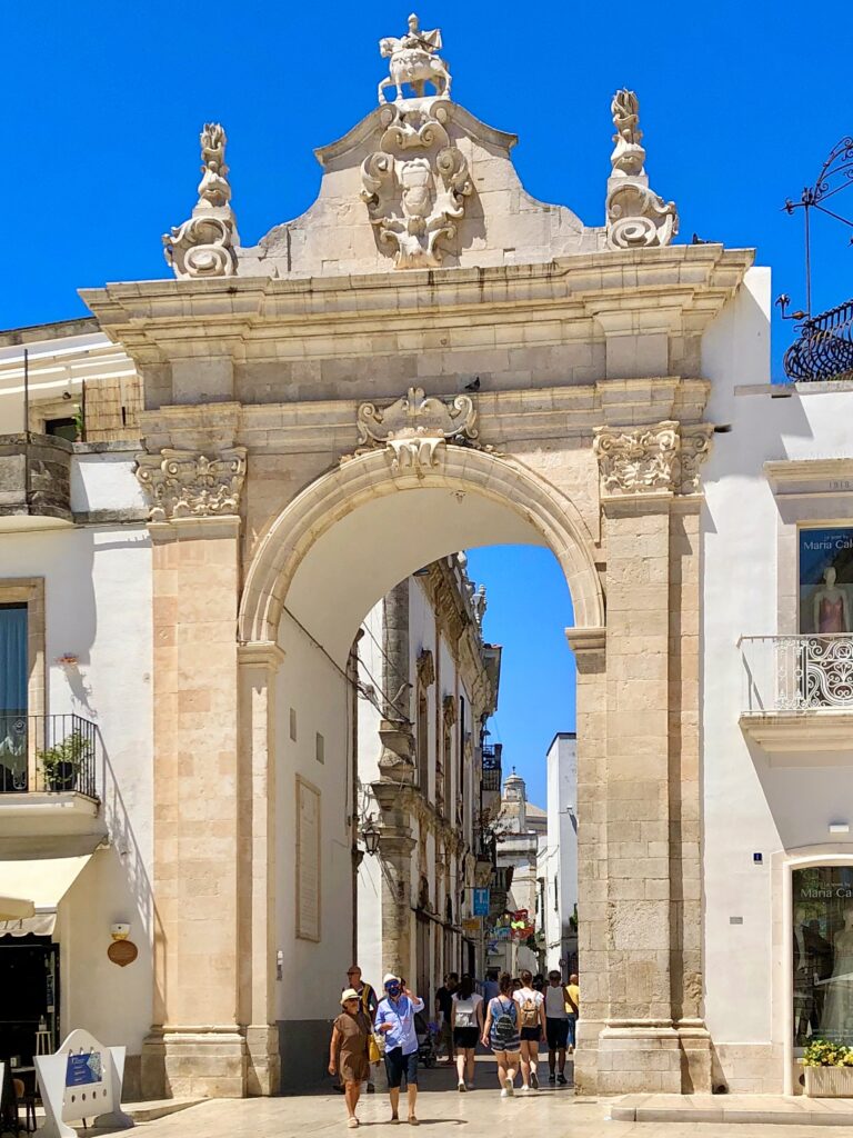 Porta Santo Stafano, Martina Franca. From The Puglia Guys Martina Franca Guide.

Martina is a town rich in Baroque elegance, historic charm, and cultural heritage. Walking through its winding streets, visitors encounter stunning churches, grand palaces, and picturesque piazzas, each telling a story of the town’s rich past. Our Puglia Guys Martina Franca guide takes you on a journey through the most remarkable sites, from the Gothic convents to the Baroque splendor of its churches and palazzi, with recommendations for the best local restaurants to complete your experience

Nestled in the picturesque Valle d’Itria, approximately halfway between the Ionian and Adriatic Seas, Martina Franca’s strategic position—which allowed for control over trade and commerce, a key factor in the town’s prosperity—played a crucial role in shaping its past, from ancient settlements to medieval fortifications and Baroque splendour. 

For history lovers, art enthusiasts, and cultural explorers, Martina’s churches offer a glimpse into a time when faith and art were inextricably linked, creating monuments that continue to inspire and captivate.

Today, Martina Franca is a vibrant town, the largest of the Valle d’Itria. Its charm lies in its baroque architecture, splendid churches, the narrow streets of its old town, and 18th-century town houses with Baroque features and wrought-iron balconies. Known for its gastronomy (we recommend some of our favourite restaurants, but in reality there is no need to adhere to it, good food is easy to find) its best known culinary export capocollo di Martina Franca (our favourite regional cured meat).

Photo by the Puglia Guys, Puglia Travel ambassadors. PugliaGuys.com
